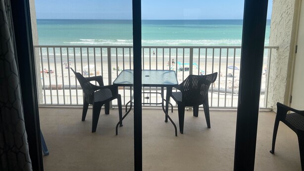 A balcony with a view of the beach, a table, and two chairs. - Castle Reef - 333 stunning direct ocean front condo on the no drive part of the beach! (New Smyrna Beach)