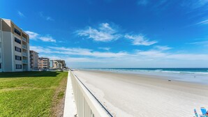 A beachfront hotel with multiple floors, a sandy beach, and a clear blue sky.
