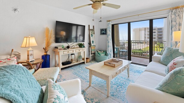 A living room with a ceiling fan, a flat-screen TV, a sofa, a coffee table, and a view of the outdoors.