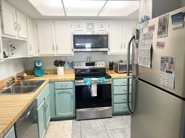 A compact kitchen with white cabinets, a stainless steel refrigerator, a microwave, an oven, and a toaster.
