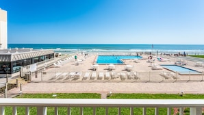 Un área de piscina en la azotea con varias piscinas, vista a la playa y un edificio con fachada de vidrio.