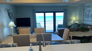 A modern kitchen with a sink, a dining area with chairs, a television, and a view of the ocean. - Castle Reef 331 ultimate ocean views! (New Smyrna Beach)
