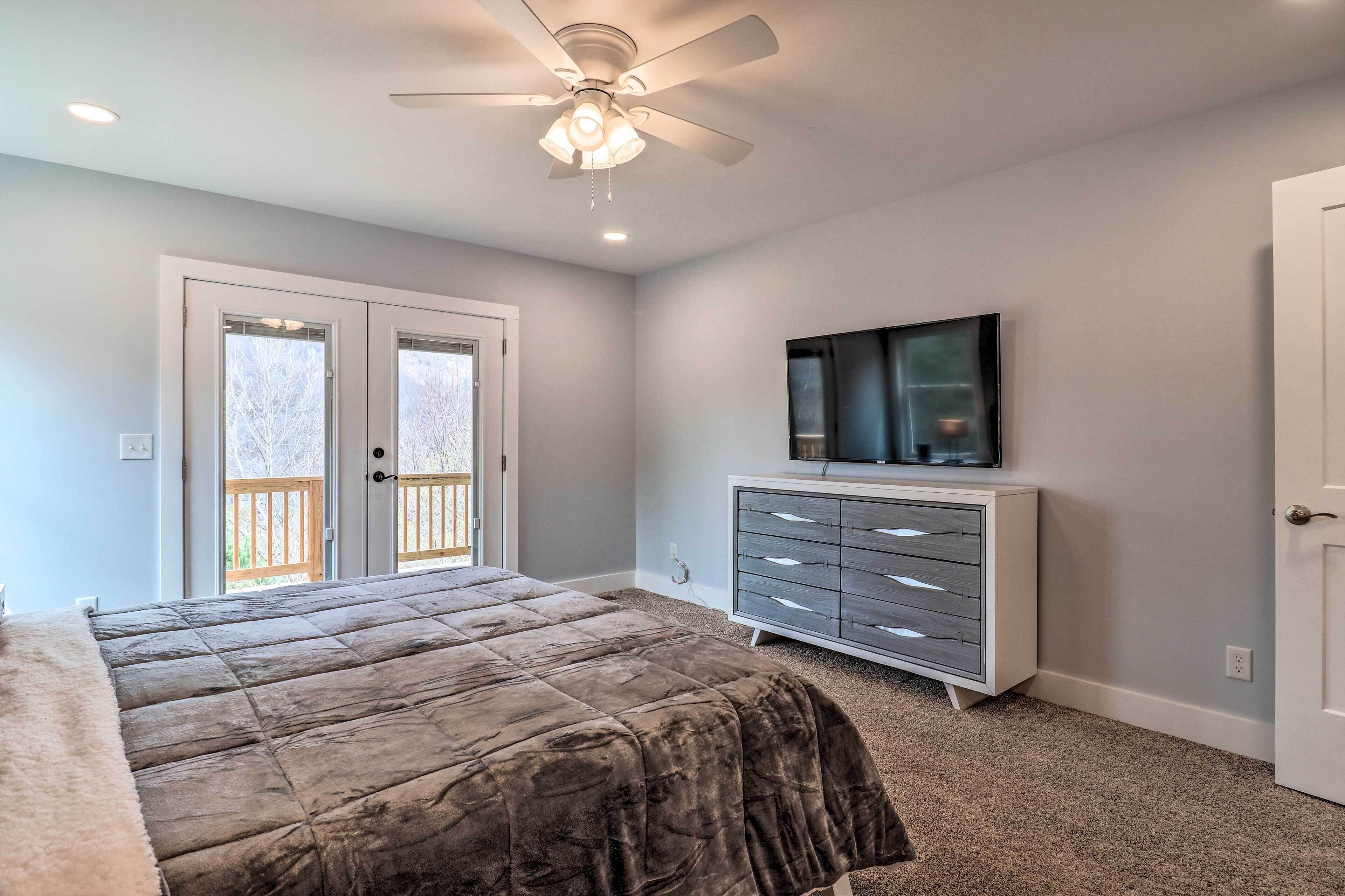 A bedroom with a bed, a ceiling fan, a dresser, and a television on the wall.