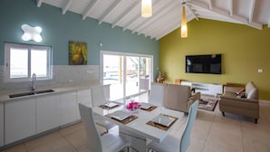 A modern kitchen with white cabinets, a dining area with a table set for two, and a living area with a sofa and TV.