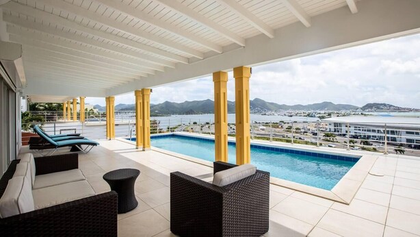 A poolside area with lounge chairs and a view of the sea and mountains.