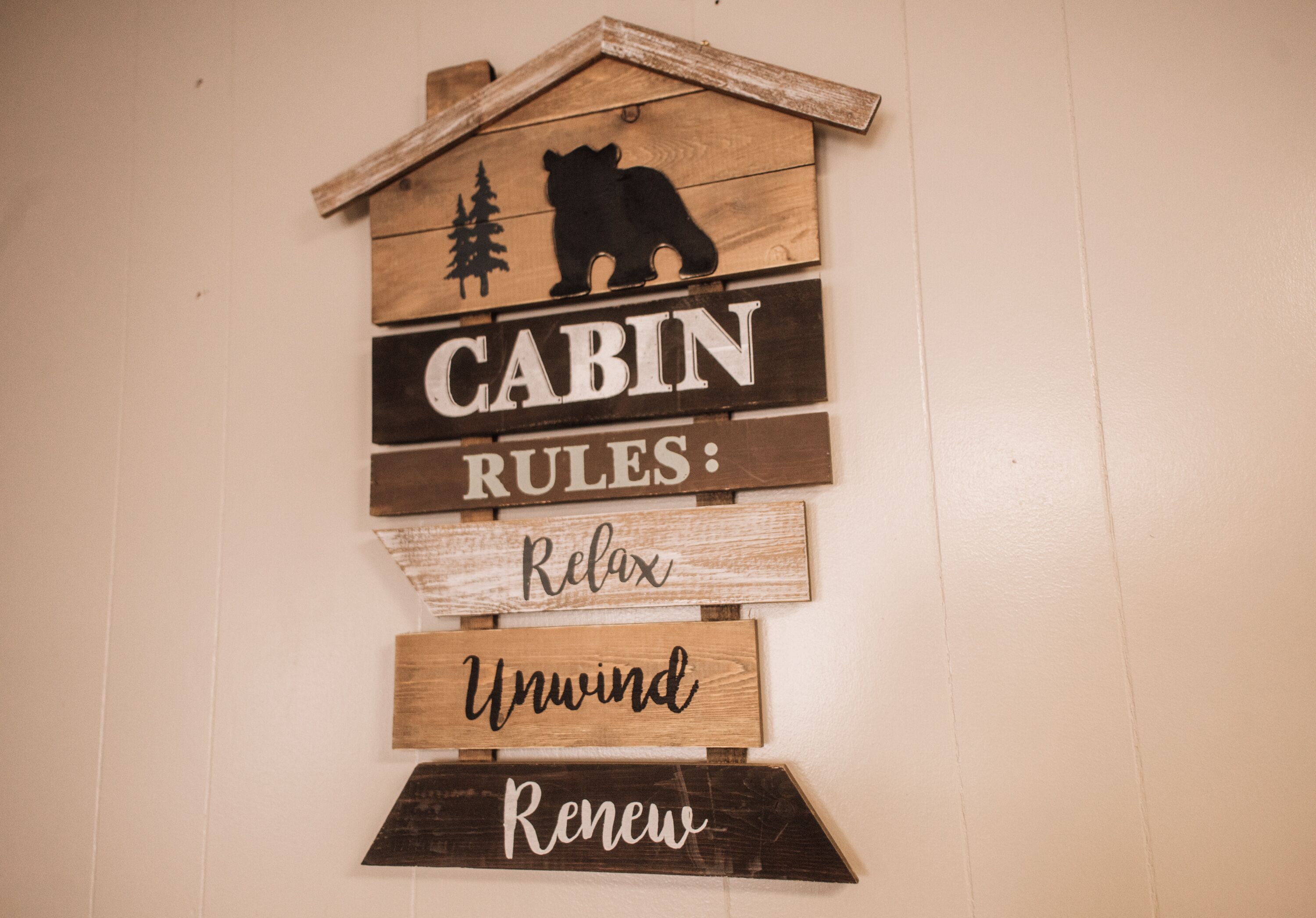 A wooden cabin-themed sign with the words "CABIN RULES: Relax, Unwind, Renew" and a bear silhouette.