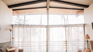 A room with a wooden ceiling, a large window with sheer curtains, a sofa, a chair, and a floor lamp. - Multi-Family Cabin @ Shenandoah Bryce Resort (Basye)