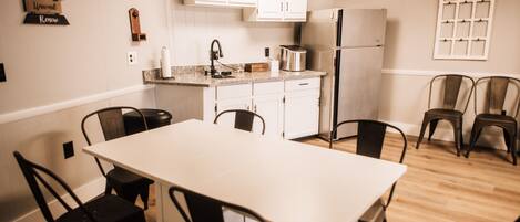A modern kitchen with white cabinets, a stainless steel refrigerator, a toaster, and a dining table with chairs.