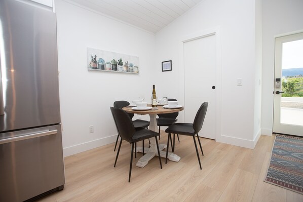 Una cocina moderna con un refrigerador de acero inoxidable, una mesa de comedor de madera con cuatro sillas y una planta en maceta en la pared.