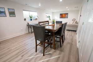 Un coin repas avec une table et des chaises en bois, un canapé et une fenêtre avec des stores.