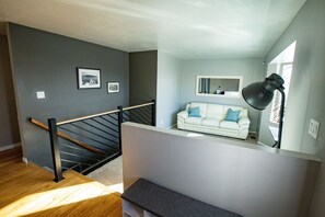 Un salon moderne avec un escalier, un canapé blanc agrémenté de coussins bleus, un lampadaire noir et un tableau encadré accroché au mur.