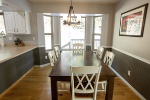 Un coin repas avec une table en bois et des chaises blanches, un luminaire suspendu et une vue dégagée grâce à de grandes fenêtres.