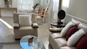Ein Wohnzimmer mit einem beigen Sofa, einem Glastisch und einem runden Beistelltisch mit Spiegel.