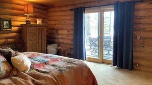Quarto acolhedor de cabana de madeira, com cama, penteadeira e janela com cortinas.