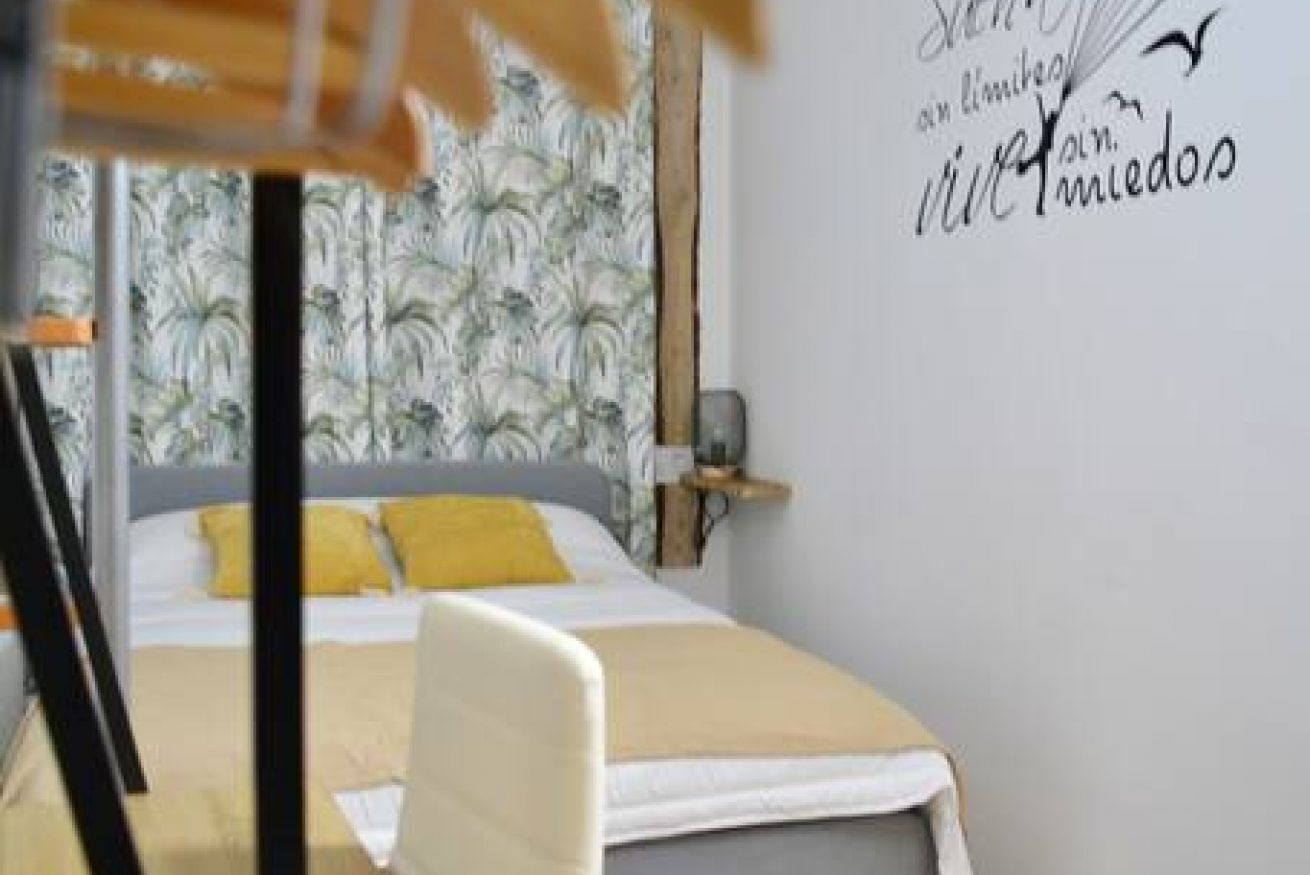 A bedroom with a bed, a nightstand, and a wall with a decorative sign.