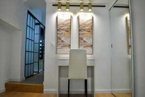A hallway with a white chair, two large abstract paintings, and a staircase leading to another room.
