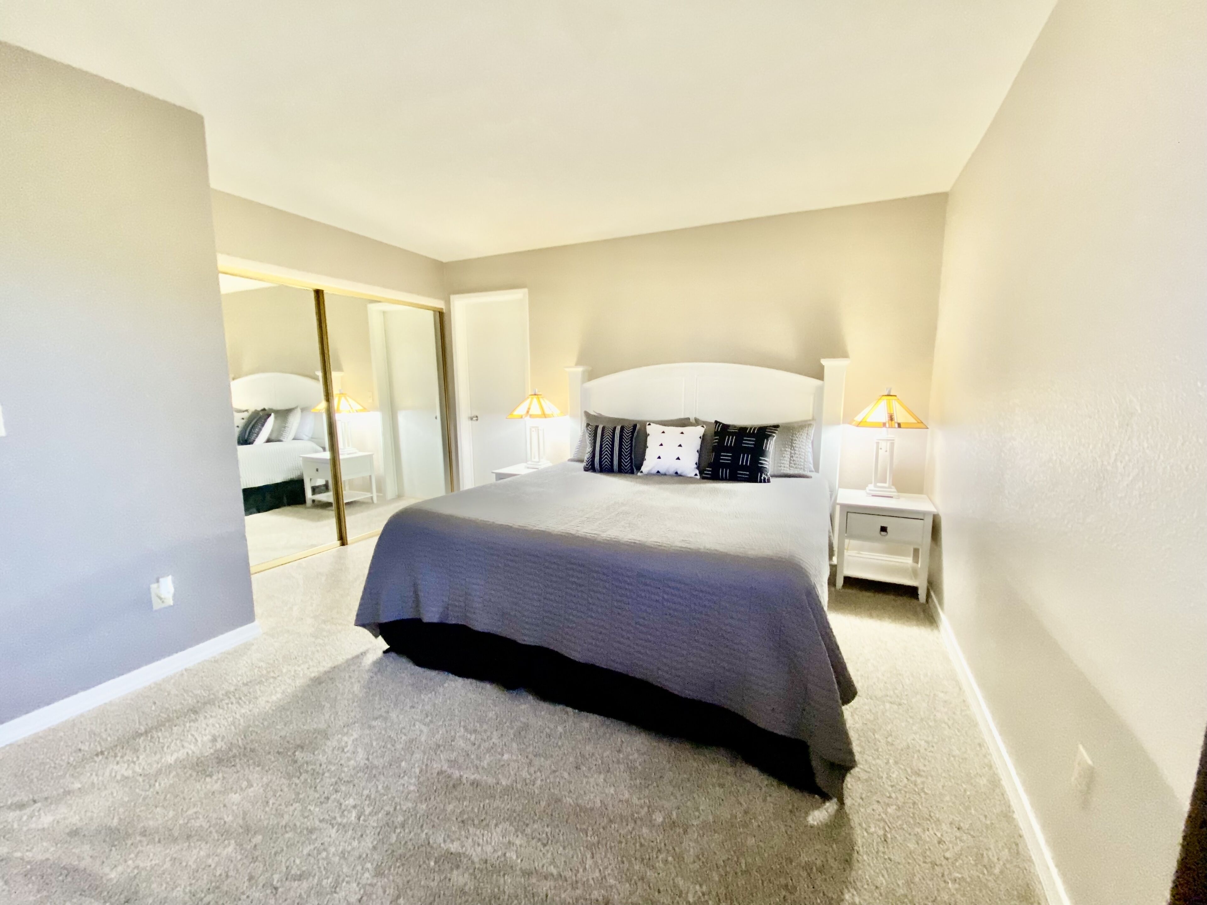 A bedroom with a large bed, a nightstand, a lamp, and a mirror.
