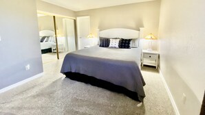 Een slaapkamer met een groot bed, een nachtkastje, een lamp en een spiegel.