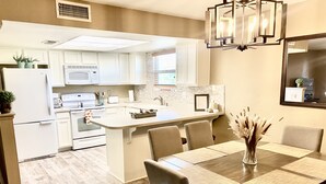 Een moderne keuken met witte kastjes, een centraal eiland en een eetgedeelte met een houten tafel en stoelen.