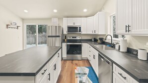 A modern kitchen with white cabinets, stainless steel appliances, and a wooden floor.