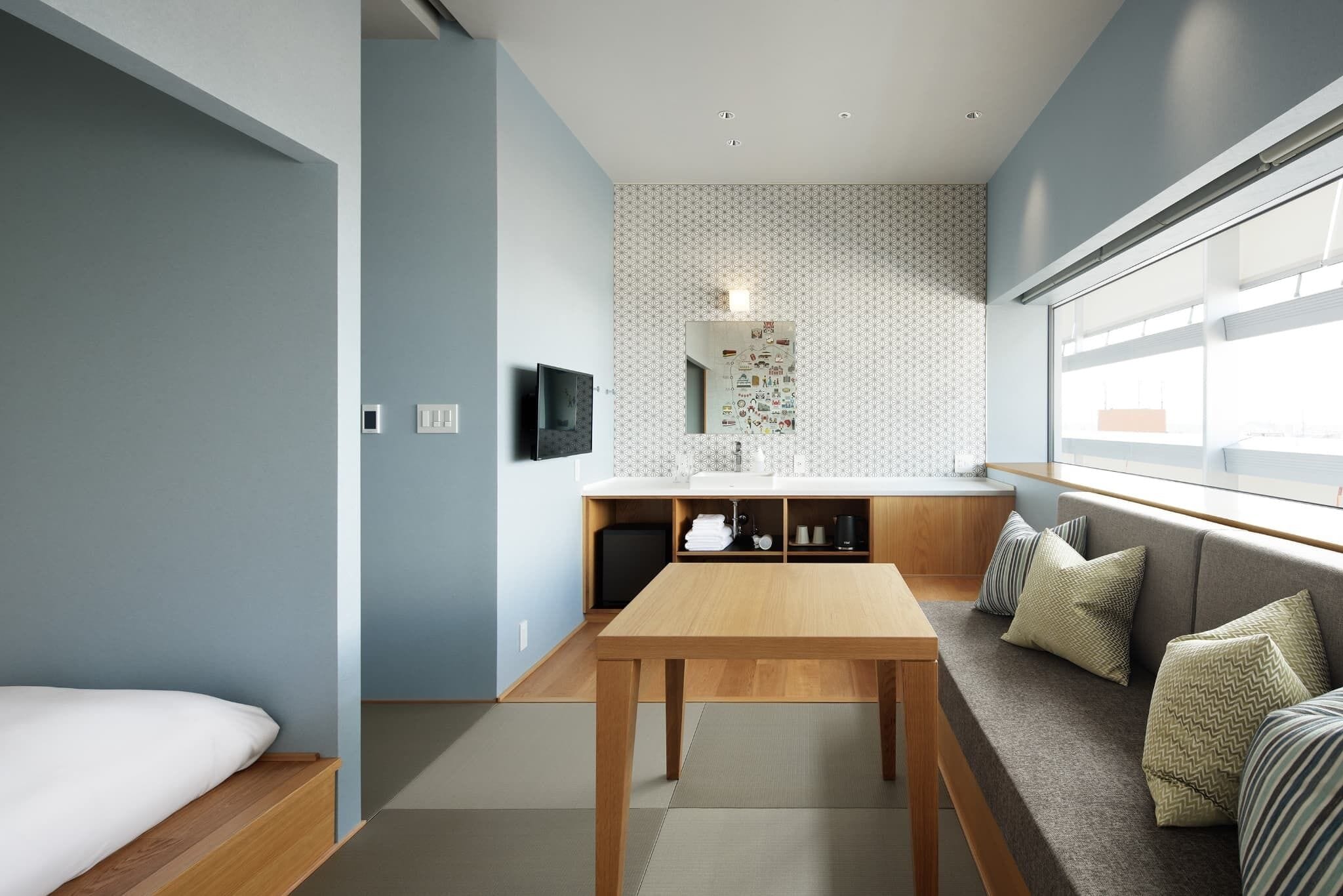 A modern interior with a wooden dining table, a sofa with cushions, a patterned wall, and a window.