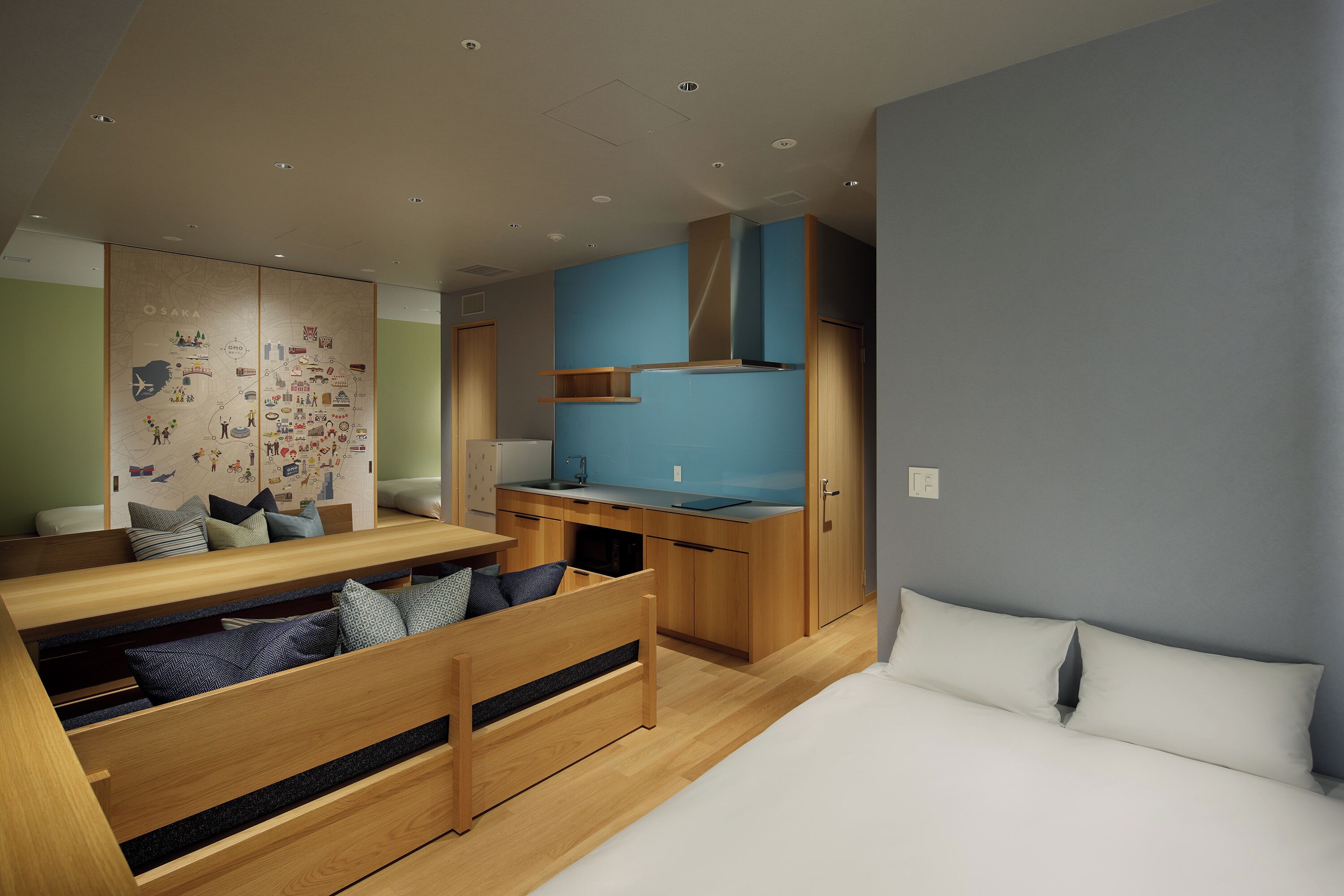 A compact bedroom with a bed, a desk, and a kitchenette.