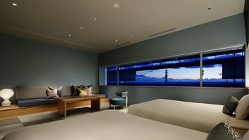 A modern bedroom with a large bed, a sofa, a small table, and a window with a view of mountains.