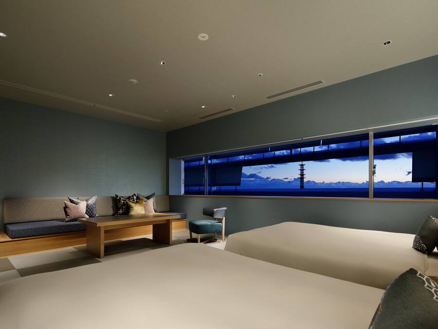 A modern bedroom with a large bed, a sofa, a small table, and a window with a view of mountains.