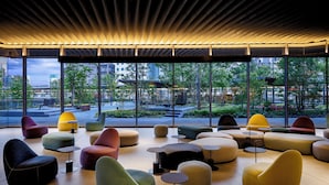Ein moderner Loungesesselbereich mit unterschiedlichen Sitzgelegenheiten, großen Fenstern mit Blick auf die Stadt und einer Decke mit einem einzigartigen Holzlamellen-Design.