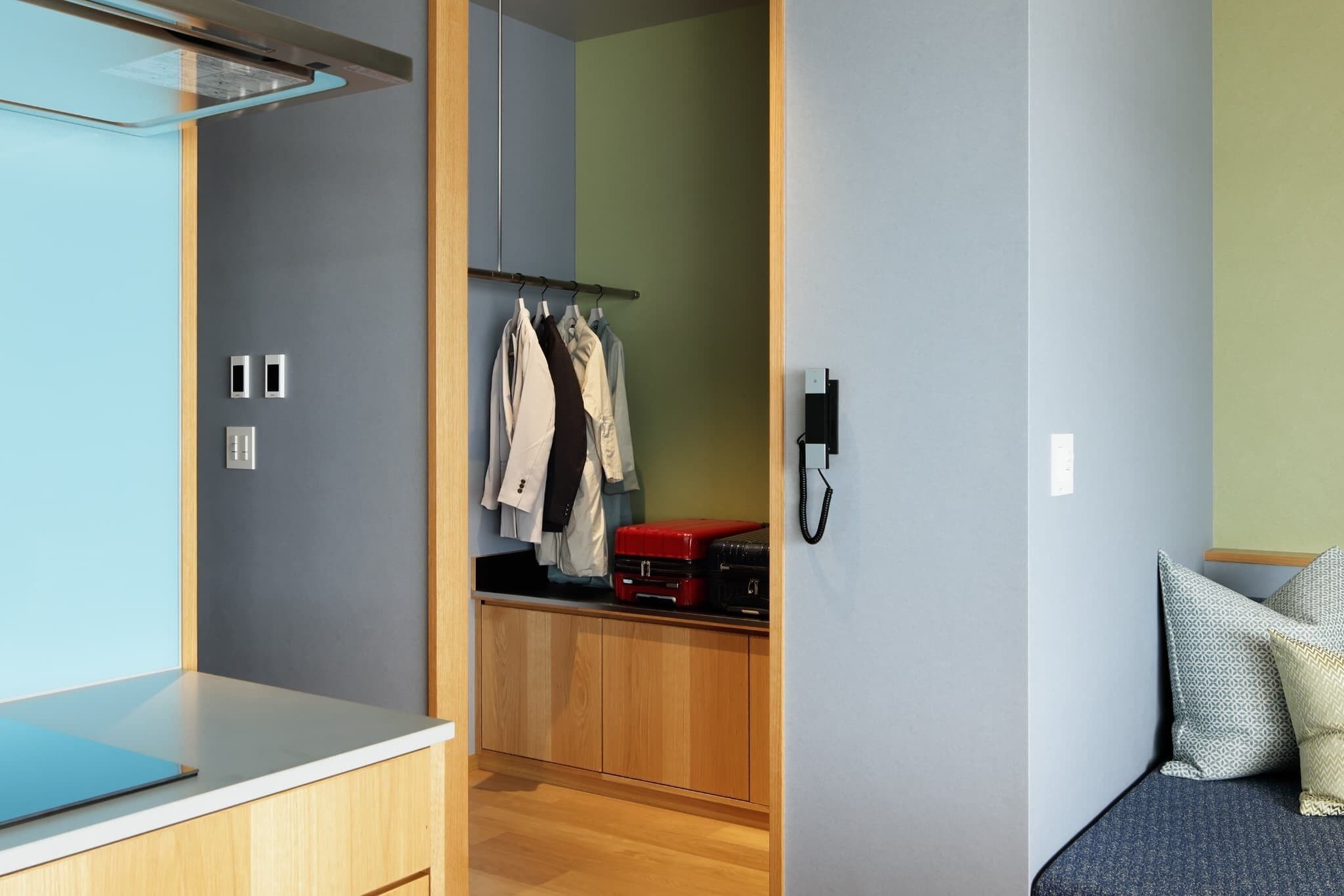 A compact room with a bed, a small desk, a wardrobe, and a closet with hanging clothes.