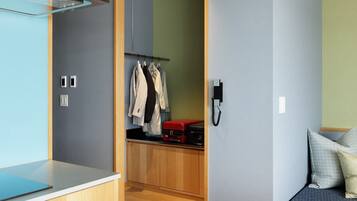 A compact room with a bed, a small desk, a wardrobe, and a closet with hanging clothes.