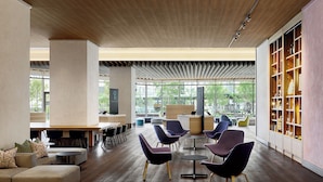 Ein großzügiger Innenbereich mit Holzbalkendecke, großen Fenstern und modernen Möbeln, darunter violette Stühle und ein Sofa.