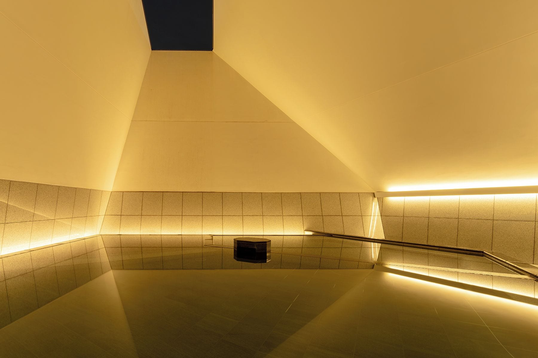 Un espacio interior moderno y bien iluminado con un diseño geométrico en el techo, paredes de azulejos y piso reflectante.
