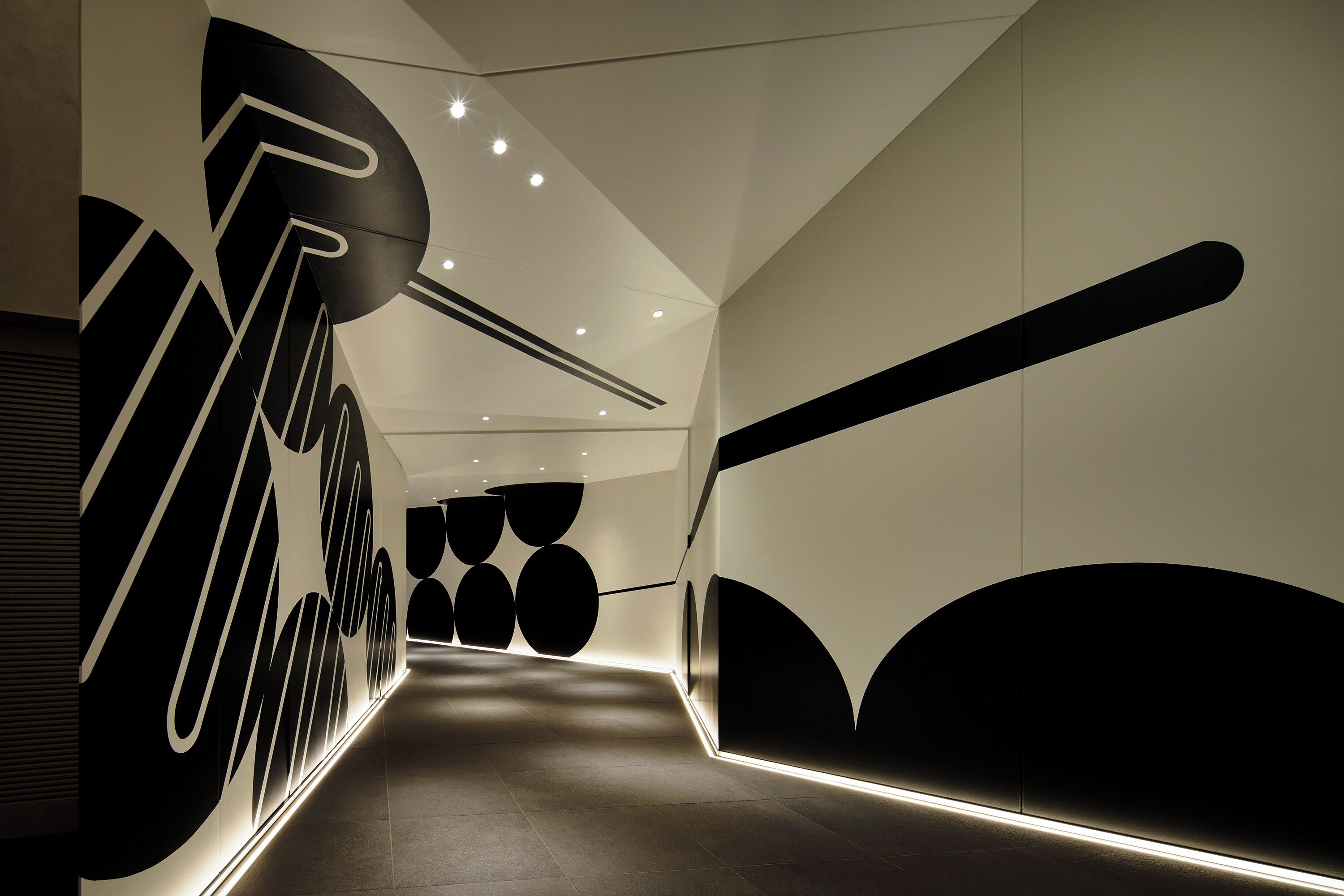 Um corredor moderno com desenhos geométricos nas paredes e iluminação embutida.