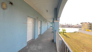 Ein langer Korridor mit Türen, ein Balkon mit Geländer und ein Blick auf ein Gewässer sowie Gebäude in der Ferne.