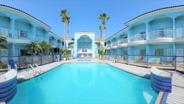 Ein Hotel mit einem zentral gelegenen Pool, mehreren Balkonen und Palmen.