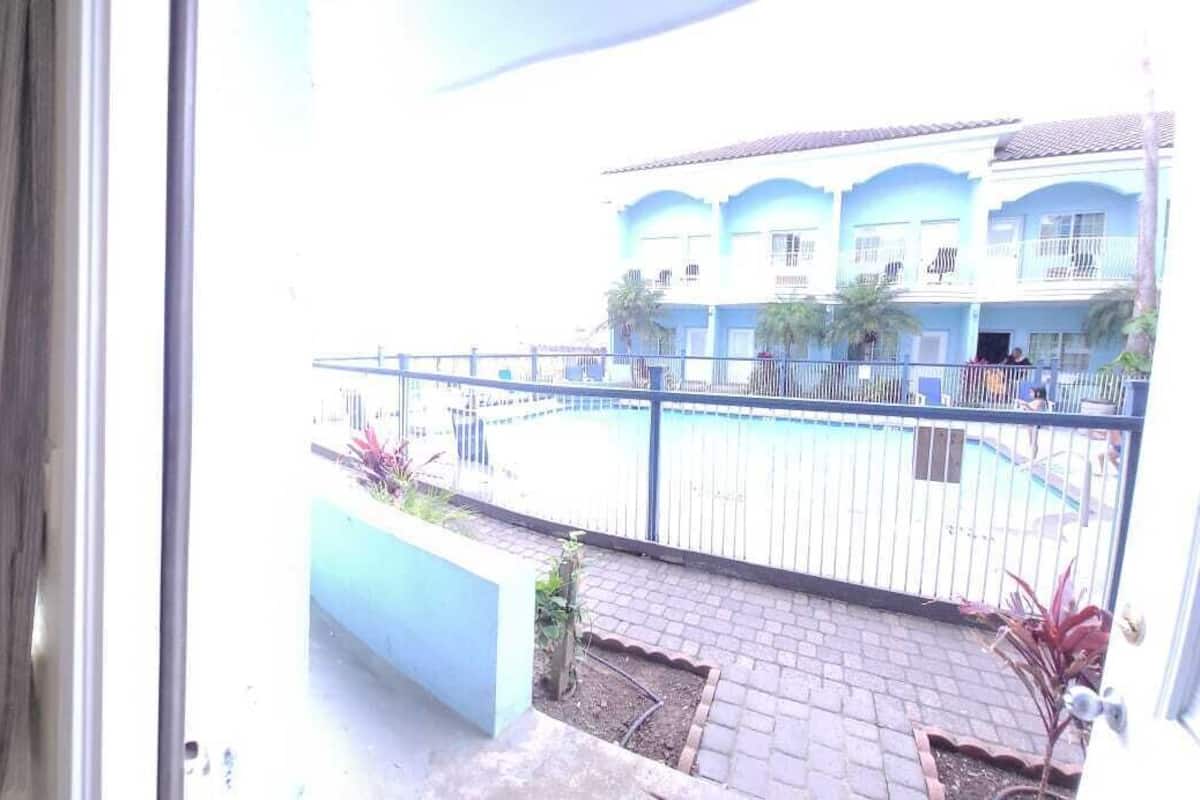 Habitación de hotel con cama, sofá y balcón con vista a la piscina y al edificio.