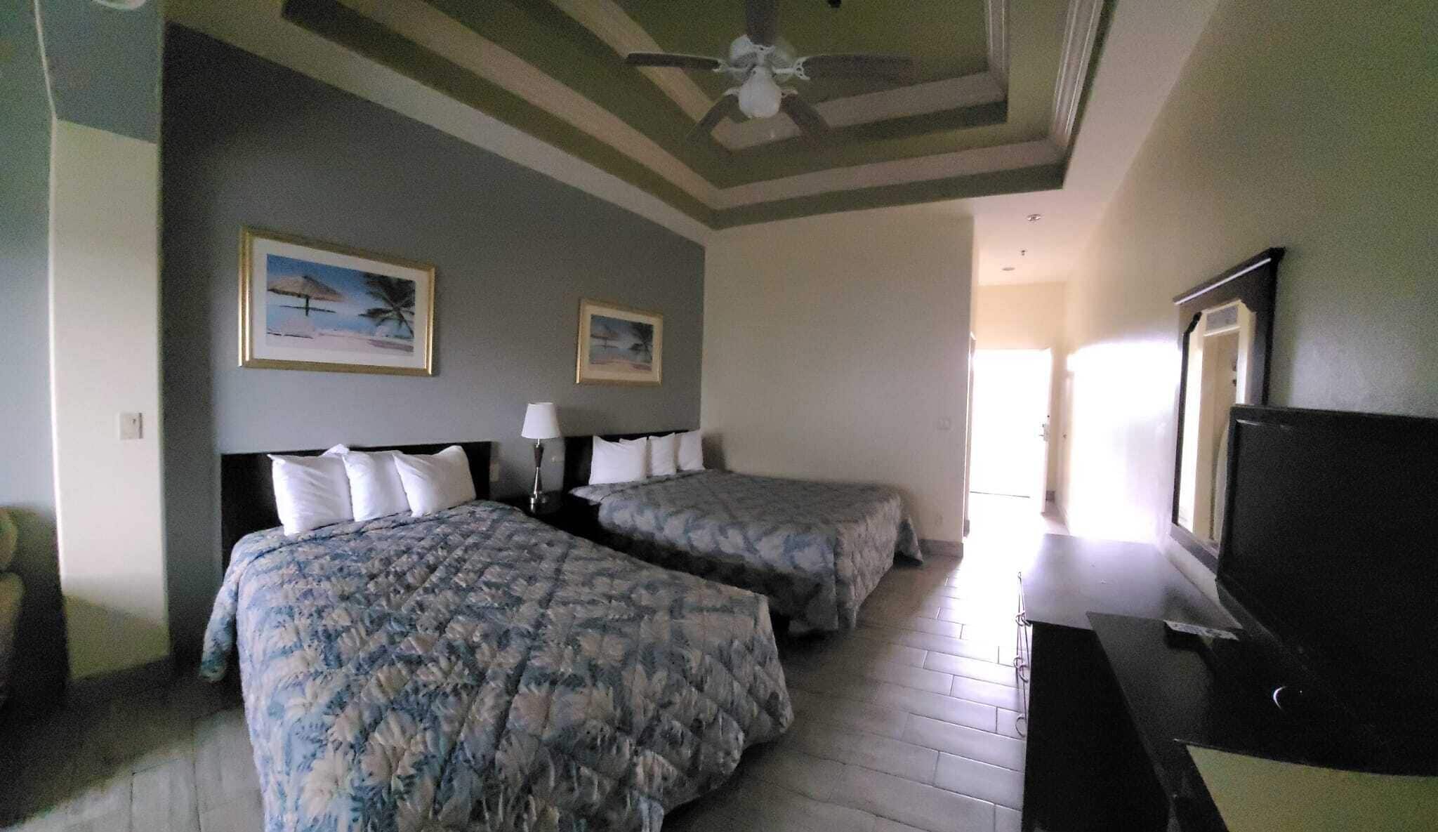 A hotel room with two beds, a ceiling fan, and artwork on the walls.