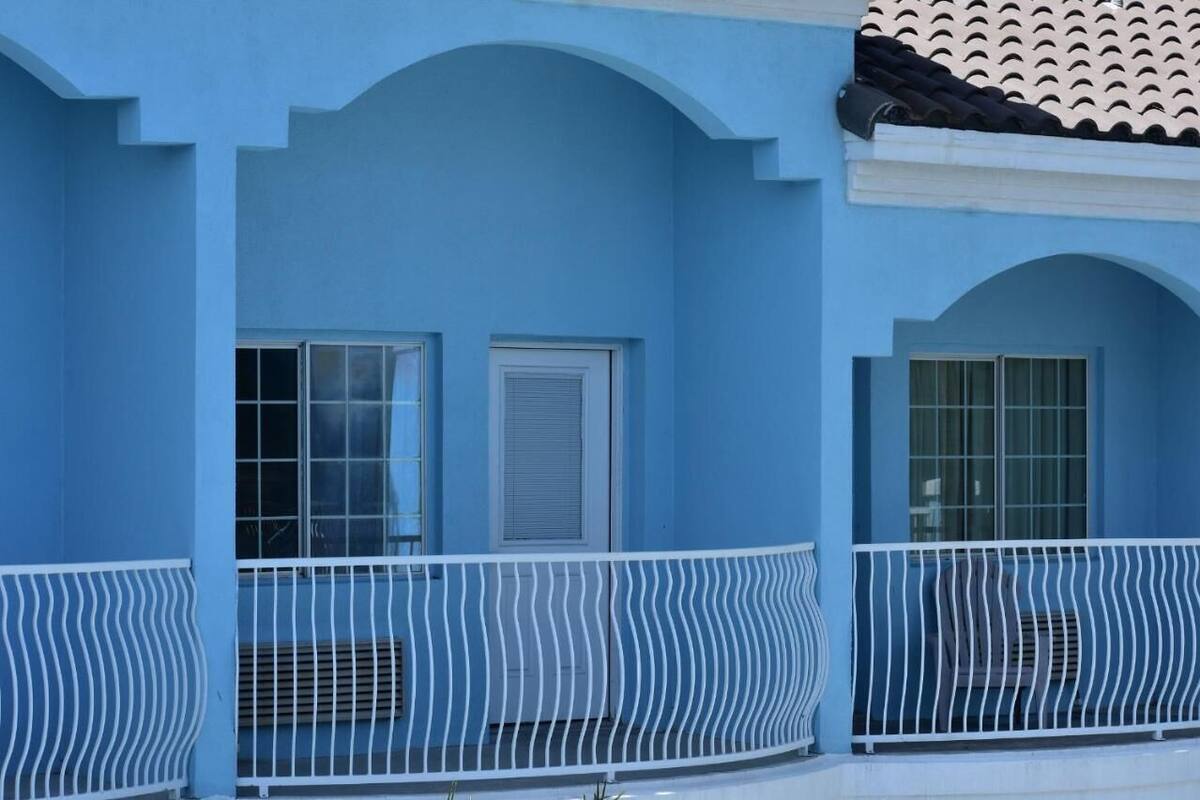 Un edificio azul con dos ventanas y una barandilla de balcón blanca.