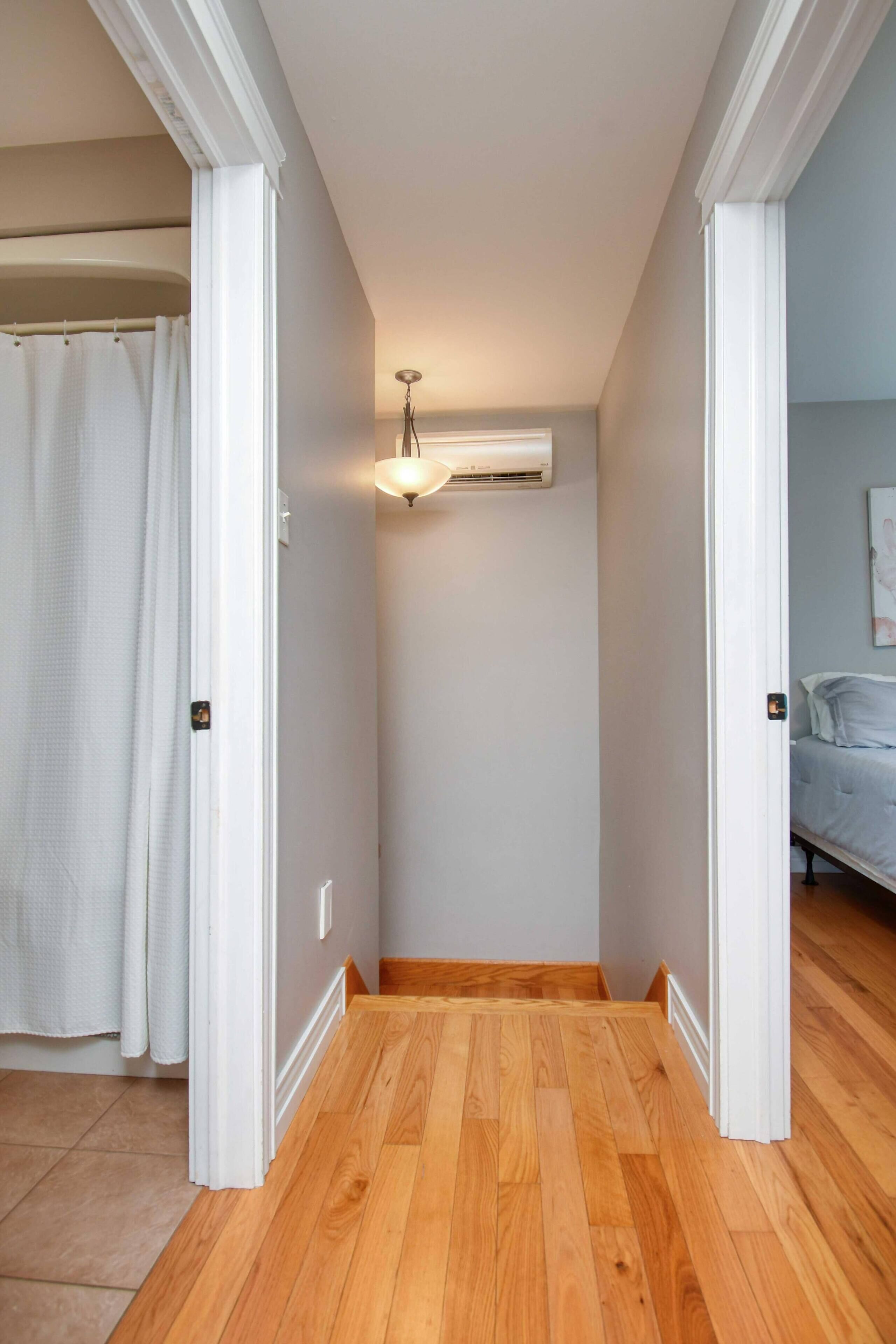 A hallway with wooden flooring, white walls, and a ceiling-mounted air conditioning unit.