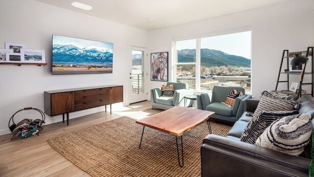 Una sala de estar moderna con un ventanal grande, un televisor de pantalla plana, una mesa de centro de madera y un sofá con cojines estampados.