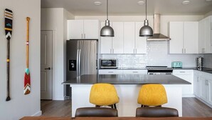 Una cocina moderna con armarios blancos, electrodomésticos de acero inoxidable y dos sillas amarillas en la isla.