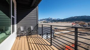 Un balcón con vistas a montañas, una terraza de madera y una barandilla.