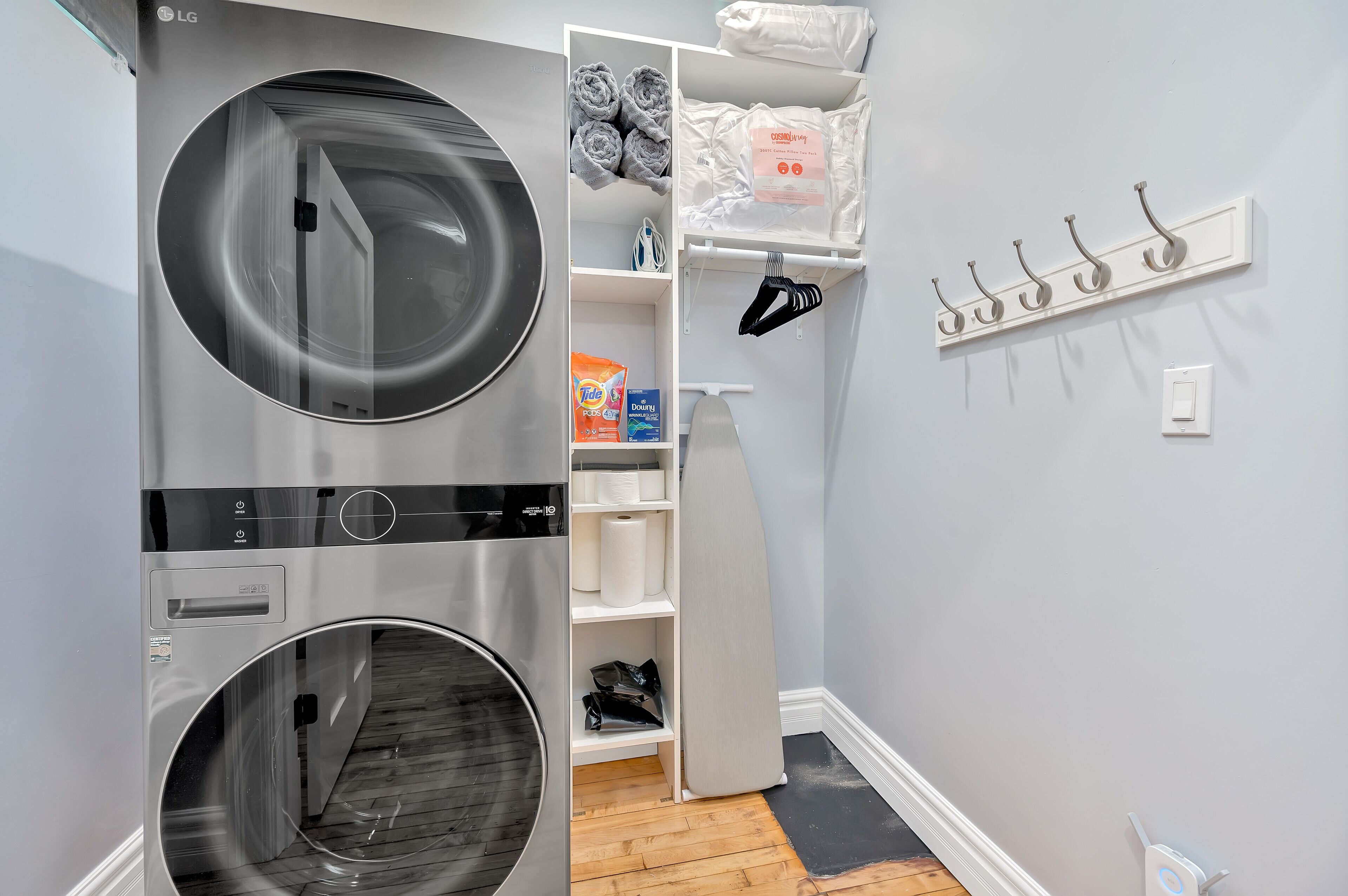 Une petite buanderie équipée d’un lave-linge et d’un sèche-linge à chargement frontal, d’une étagère avec des serviettes pliées et d’un porte-serviettes avec des crochets.