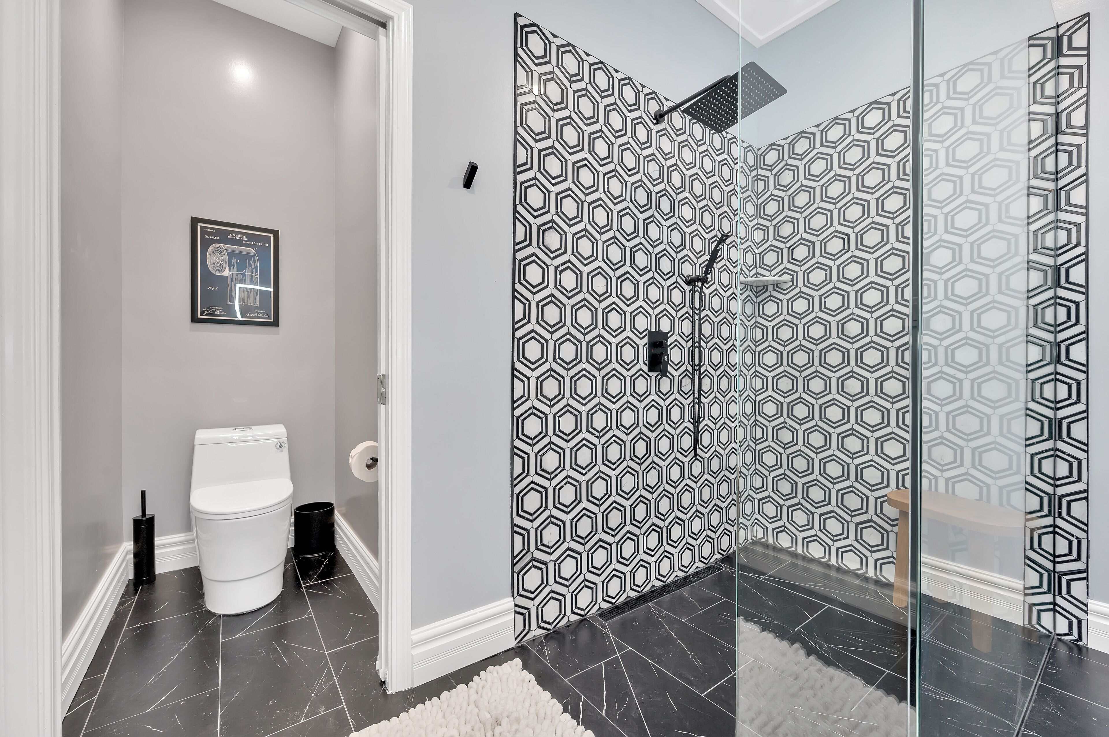 A modern bathroom with a geometric patterned shower wall, a toilet, and a framed picture on the wall.