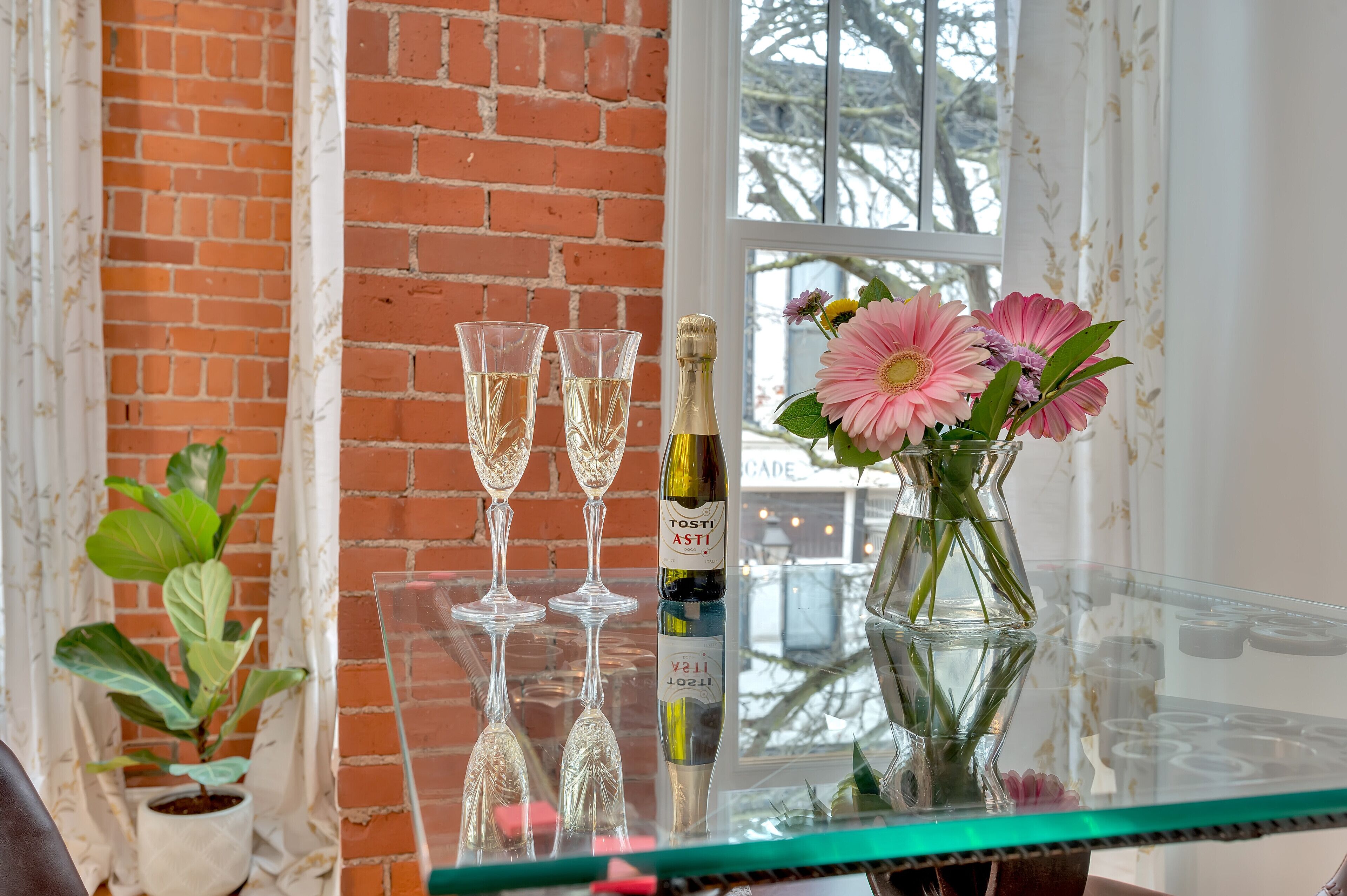 A glass table with two wine glasses, a bottle of wine, and a vase with flowers.