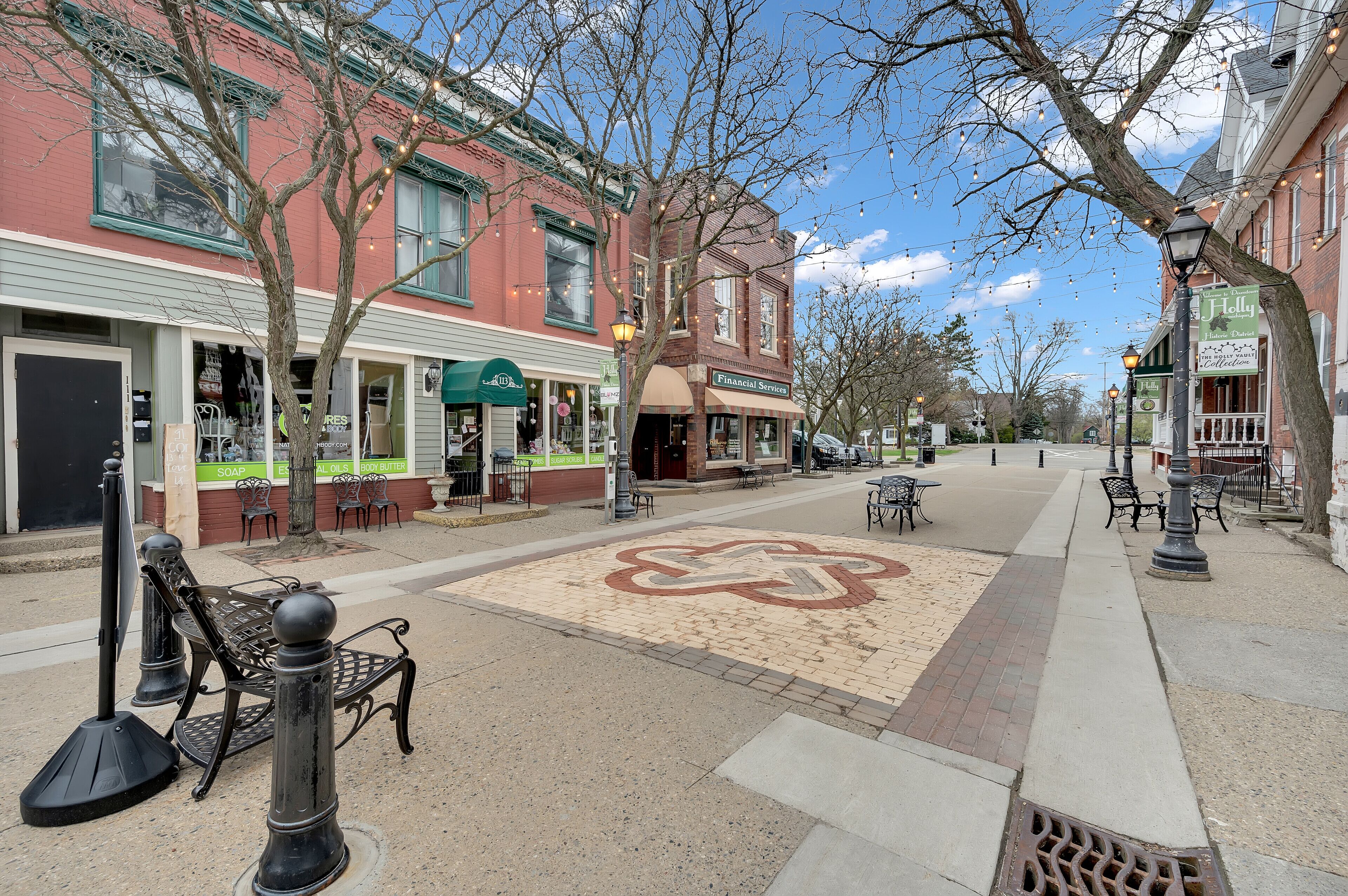 A street with brick buildings, outdoor seating, and a clear sky.