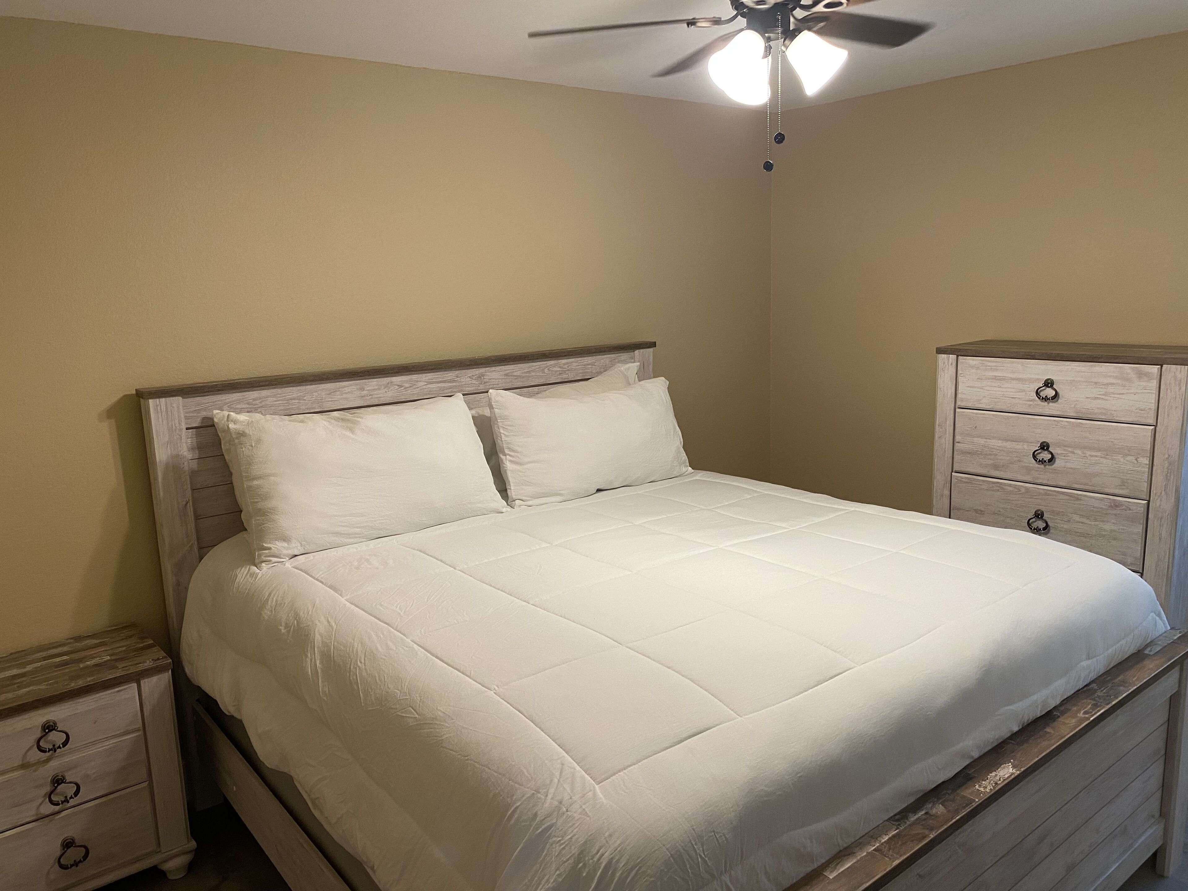 A bedroom with a bed, a nightstand, a dresser, and a ceiling fan.