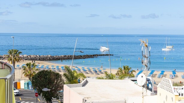 Ein Strand mit Sonnenschirmen und Liegestühlen, einem steinernen Wellenbrecher und Booten im Wasser.