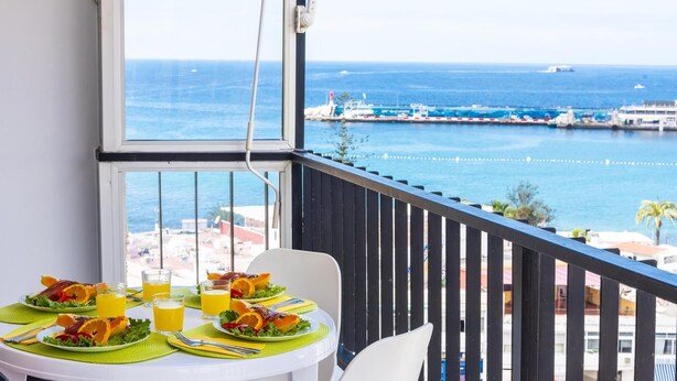 A balcony with a table set for breakfast, overlooking a marina with boats and a clear view of the sea.
